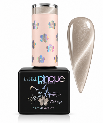 Tickled Pinque Cosmetics 'Cat eye' gel nail polish bottle with a black base and a pale pink cap decorated with iridescent flowers, shown next to a nail swatch displaying the shimmering metallic beige-pink finish.