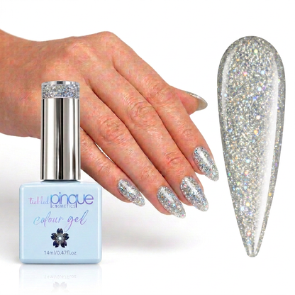 A hand with glittery silver nail polish is shown beside a bottle of Tula Nique Colour Gel and a large nail swatch displaying the sparkling silver finish.