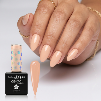 A hand with long, almond-shaped nude pink nails stands beside a bottle of Tipped Pinque Gelato nail polish and a separate nail color swatch on a clean white background.