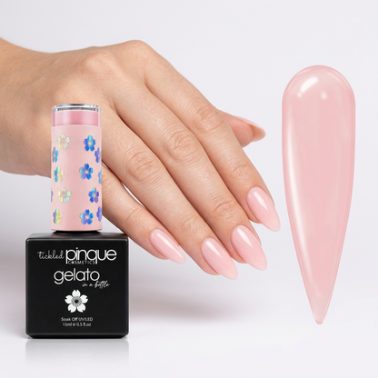 A hand with long, glossy pale pink nails is shown beside a bottle of Ticked Pinque Gelato nail polish and a large matching pink nail swatch on a clean white background.